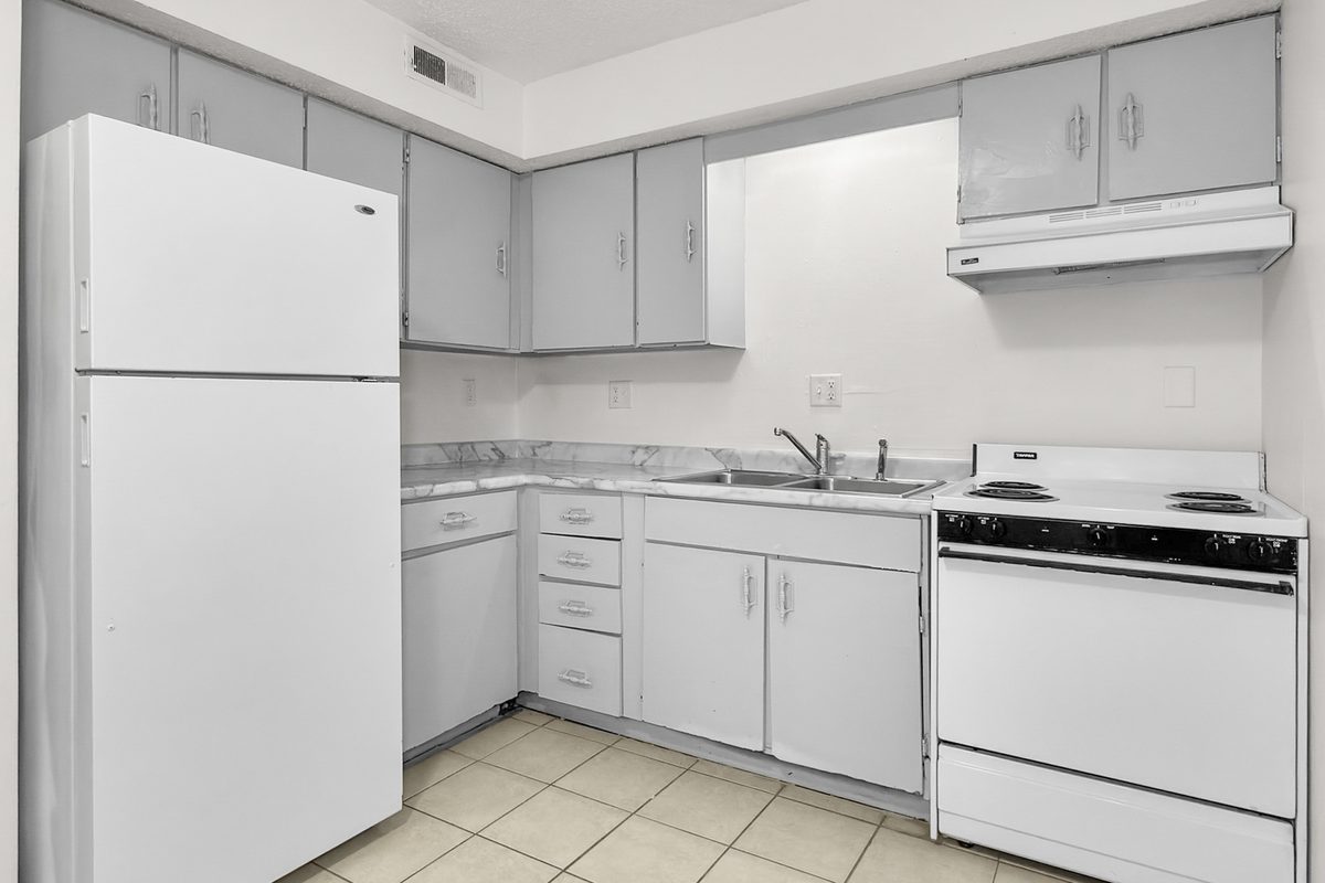 A kitchen with white cabinets, a white range and refrigerator, and a tile floor.