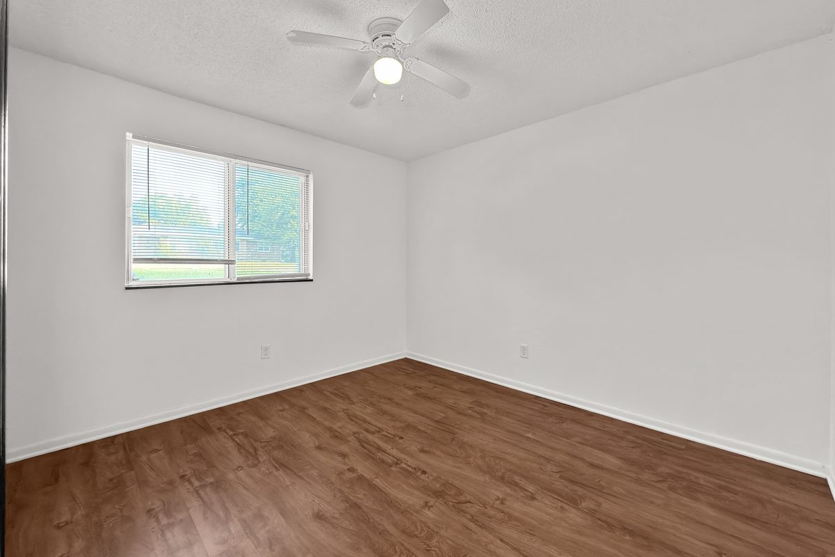 A bedroom with wood-look plank flooring, a ceiling fan and a window with blinds.