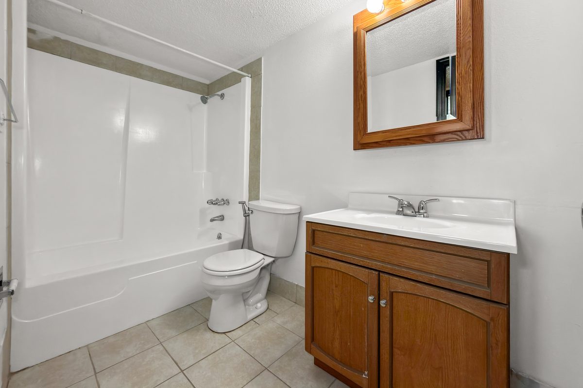 A bathroom with a tub and shower, an oak vanity with a white top and a framed mirror.
