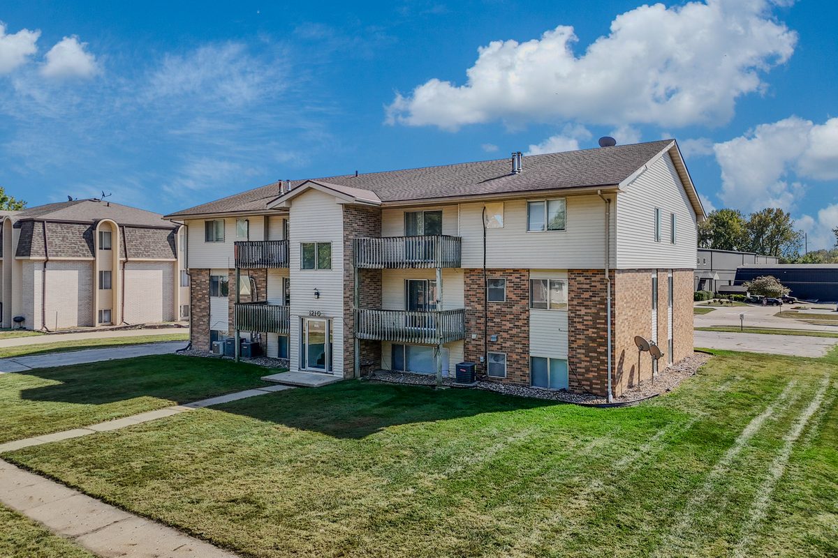 The 1210 building, three stories of cream siding over red brick with private balconies, on a wide lawn.
